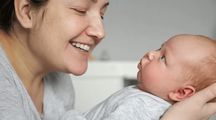 Foto de una mujer sonriendo a un bebé que sujeta entre sus manos.