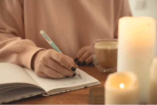 Un cuaderno sobre el que se está escribiendo, velas y un vaso de café
