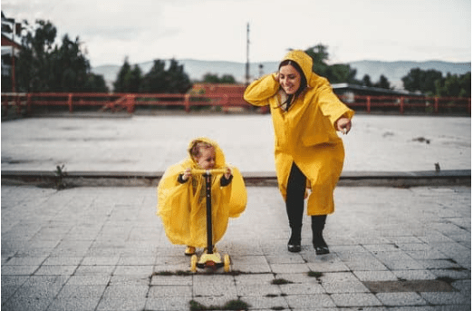 Una mujer y un niño o niña pequeño en patinete, ambos con chubasqueros a juego