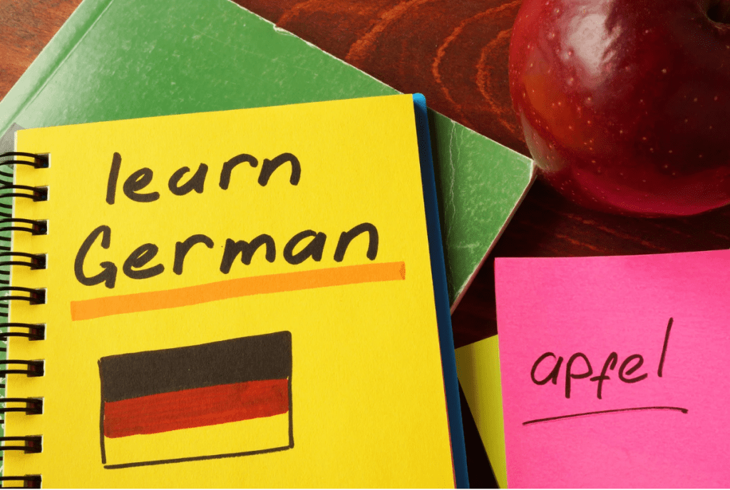 Un cuaderno que reza "learn German", y un post it con la palabra "apfel" bajo una manzana.
