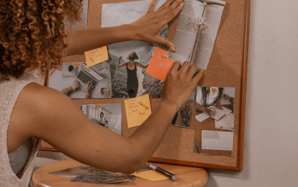 Una joven colgando fotos y notas en un tablón de corcho.