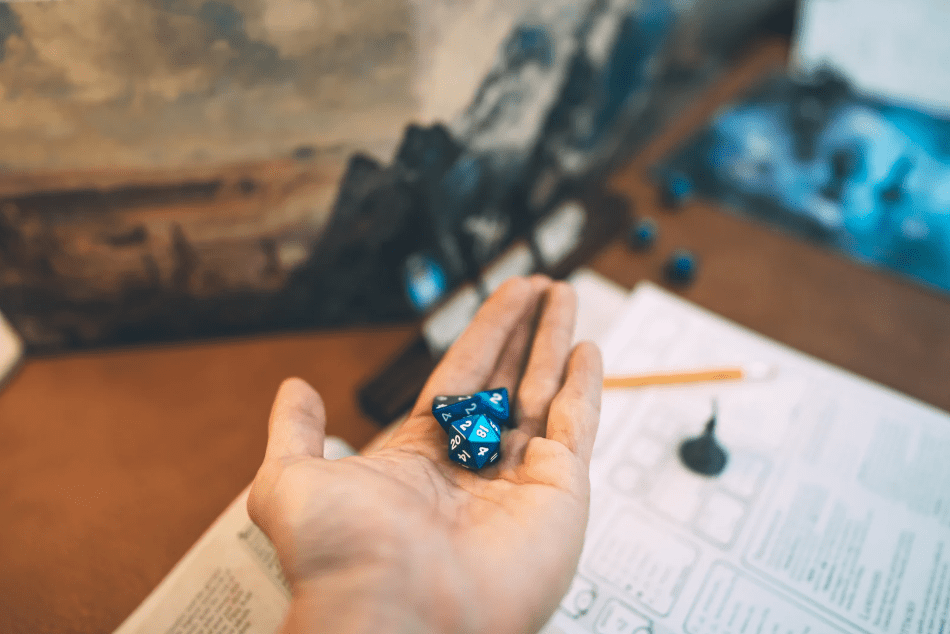 Una mano que sujeta varios dados, y material de juegos de rol como fondo.