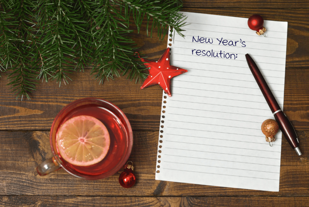 Una hoja de cuaderno arrancada que tiene escrito "New year's resolutions" con decoraciones festivas alrededor.