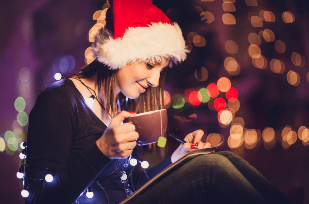 Una joven con sombrero de Navidad y una taza con té, escribiendo.