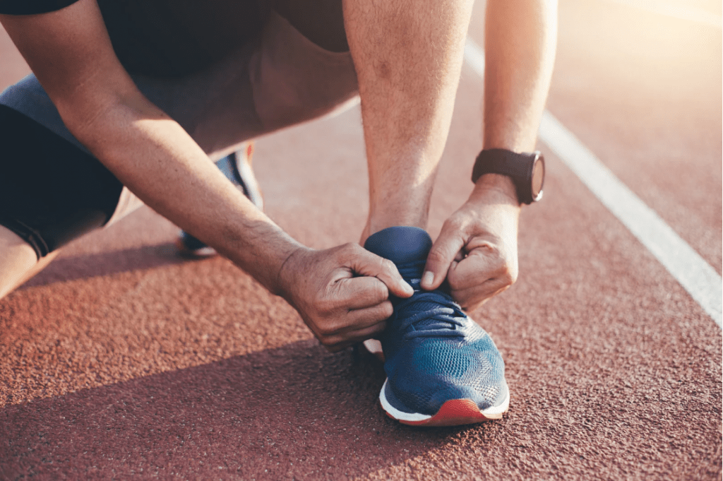 Un hombre atándose los cordones de sus zapatillas sobre una pista de correr.