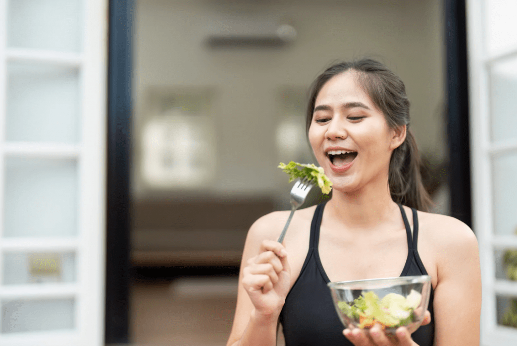 Una joven comiendo felizmente ensalada.