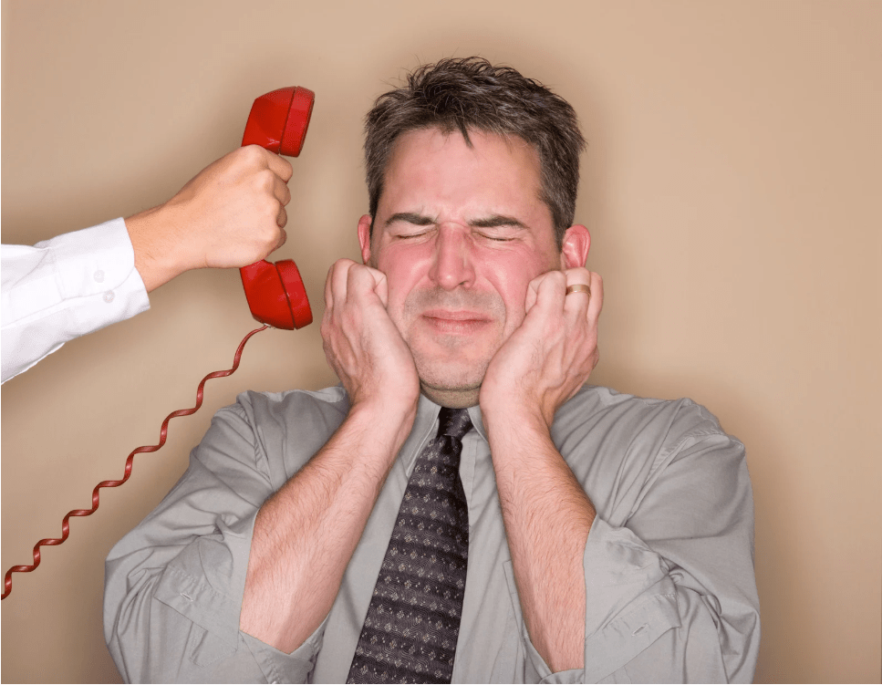 Un joven tapándose las orejas con expresión angustiada, y un teléfono siendo sujetado cerca de su cabeza.