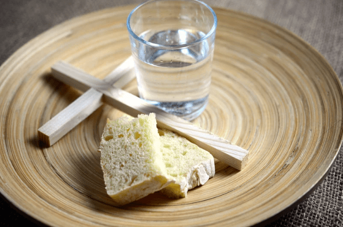 Un plato con una cruz de madera, un vaso con agua, y dos trozos de pan.