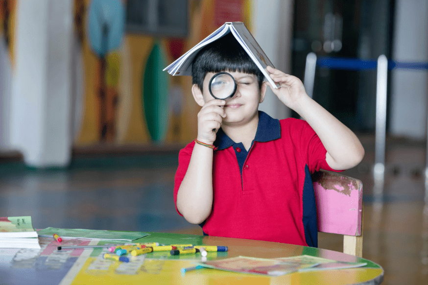 Un niño con una lupa y un libro en la cabeza.