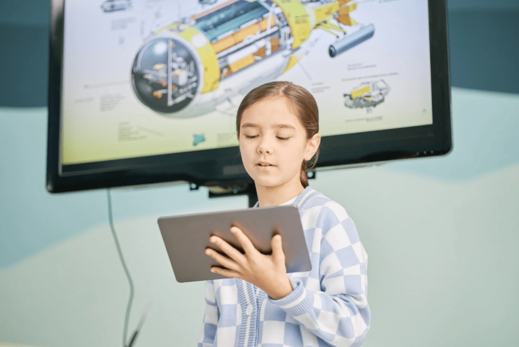 Una niña mirando a una tablet. Tras ella, un diagrama educativo.