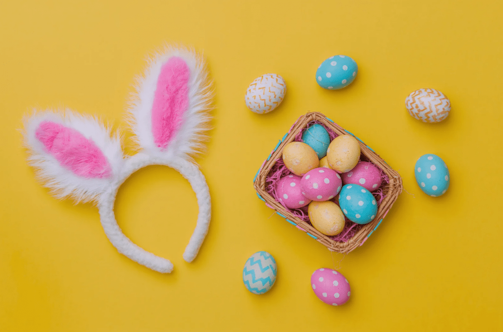 Una cesta de huevos de colores, y una diadema con orejas de conejo.