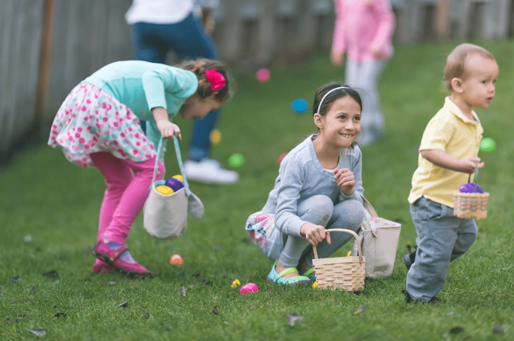 Niños y niñas recogiendo huevos de colores en un jardín.