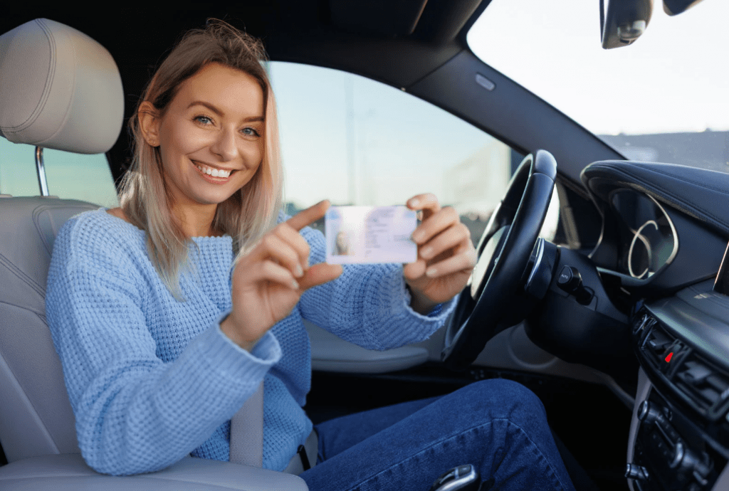 Una joven enseñando su carné desde el asiento de conductor del coche.