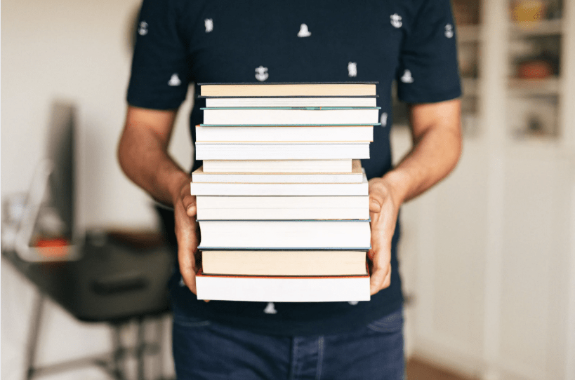 Un joven sujetando una pila de libros.