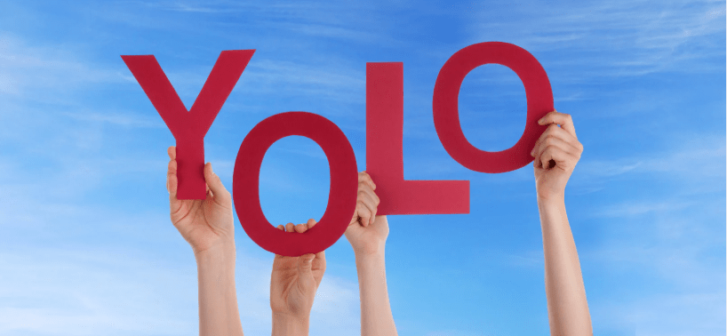Cuatro manos sujetando letras gigantes que rezan "YOLO".