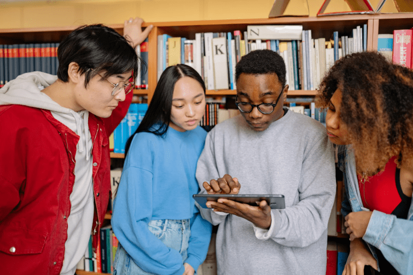 Un grupo de jóvenes en una biblioteca mirando una tablet.