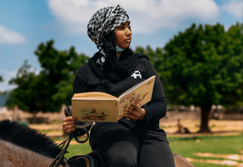 Una joven lee mientras monta a caballo en el campo.