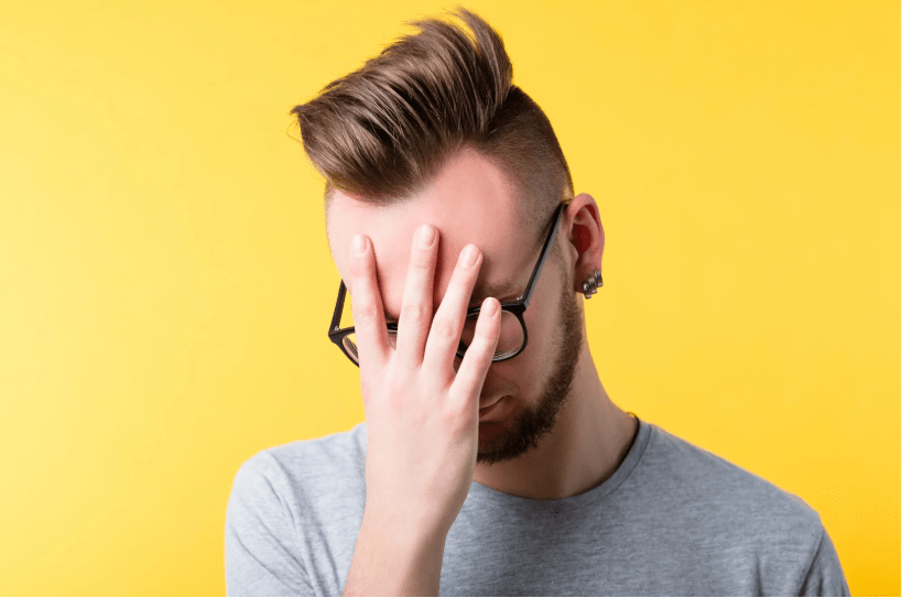 Un joven cabizbajo con una mano tapándole la cara.