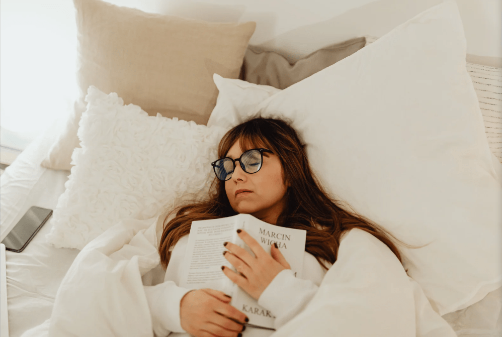 Una joven, aún con las gafas puestas, duerme abrazada a un libro abierto.